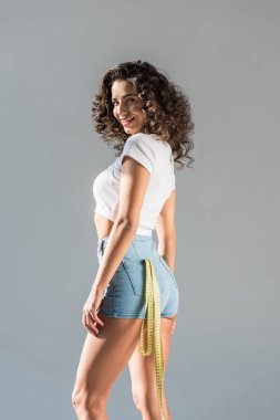 Teyp gri izole kamera bakarak cebinde ölçme ile şortlu seksi kıvırcık kız