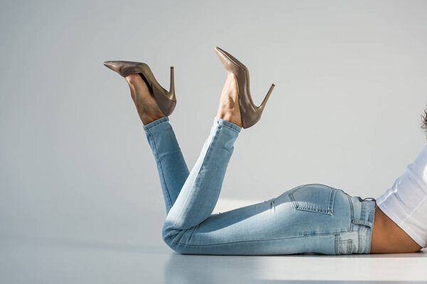 Cropped view of woman in jeans and high-heeled shoes on grey background