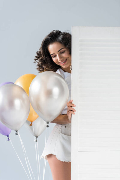 Blissful curly young woman with air balloons on grey background
