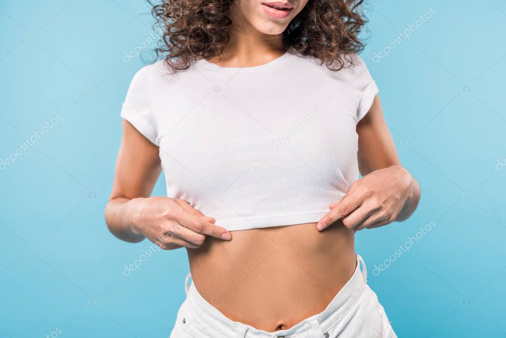 Cropped view of curly young woman in crop top on blue background