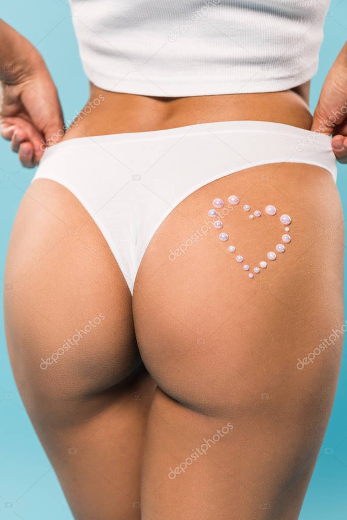 Cropped view of shapely girl in white panties with heart symbol on blue background