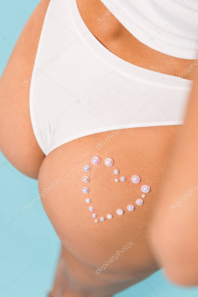 Cropped view of woman in white panties with heart sign on blue background