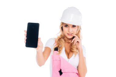 handy woman in pink overalls standing and holding smartphone with blank screen isolated on white clipart