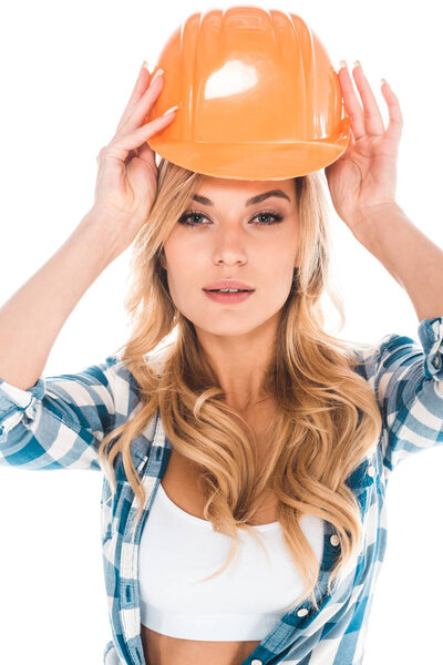blonde handy woman in blue shirt putting on orange hardhat isolated on white