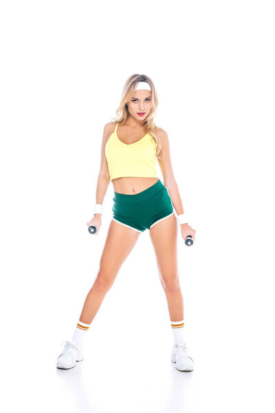 attractive blonde fitness trainer in green shorts and yellow singlet with dumbbells on white background