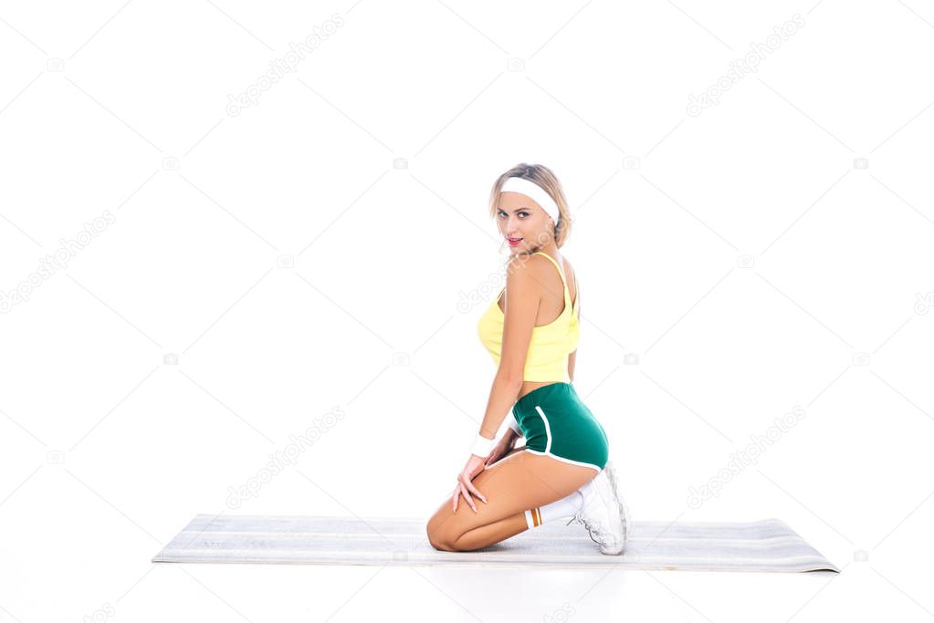 blonde fitness trainer in green shorts and yellow singlet on yoga mat isolated on white