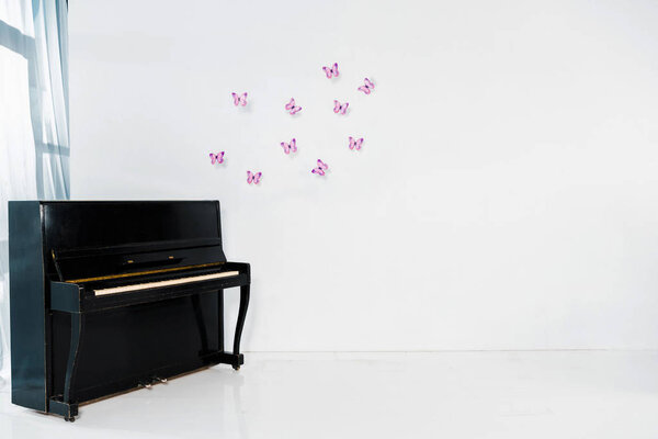 черный фортепиано на белом фоне с фиолетовыми бабочками и копировать пространство
