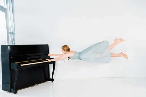 Плаваюча Дівчина Блакитній Сукні Грає Чорному Піаніно Білому Тлі — стокове фото