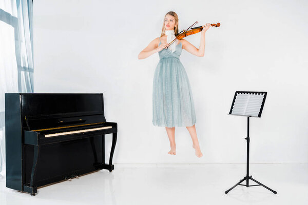 floating girl in blue dress playing violin and looking away on white background