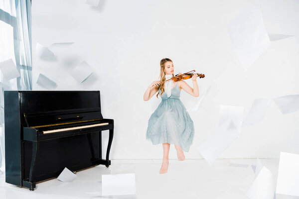 floating girl in blue dress playing violin with sheets of paper in air 