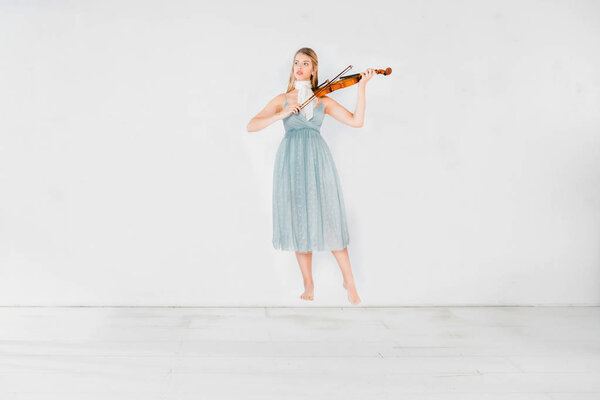 floating girl in blue dress playing violin on white background with copy space