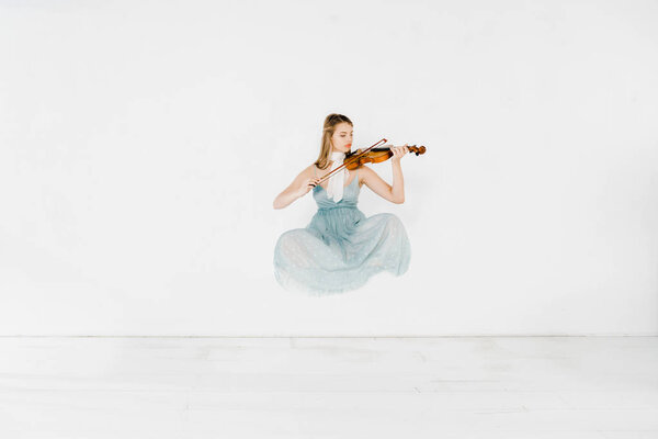 плавающая девушка в синем платье играет на скрипке на белом фоне
 