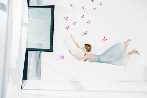 floating girl in blue dress raised hands near window