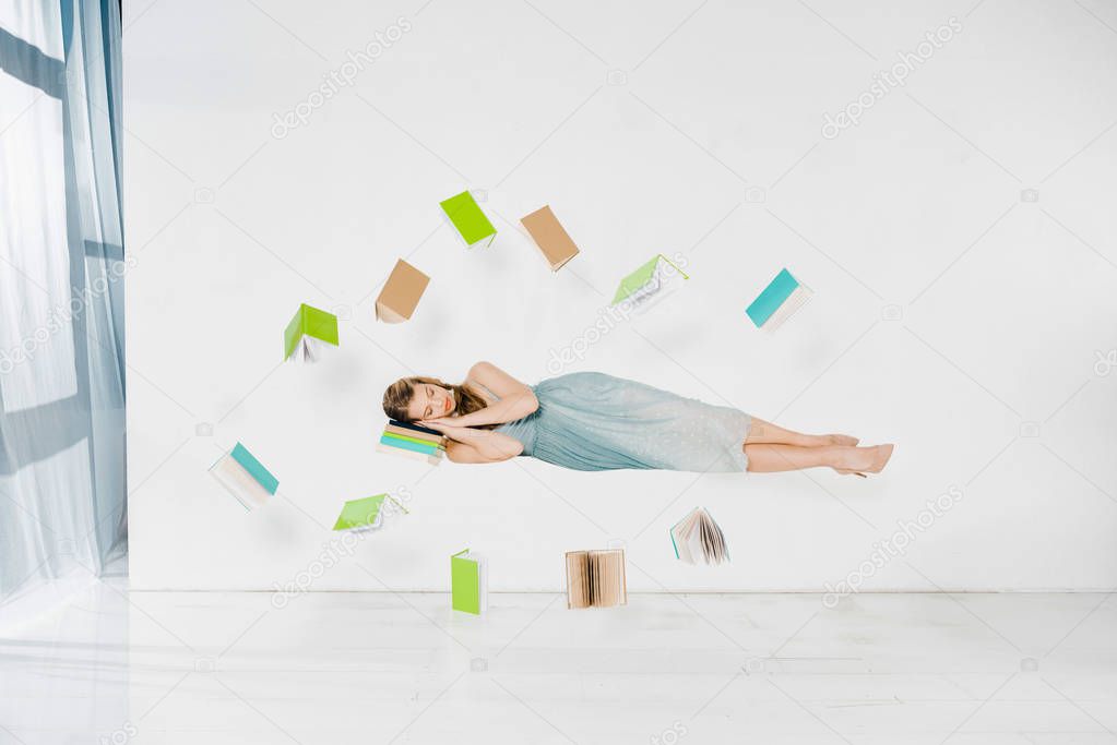 floating girl in blue dress sleeping on book in air on white background