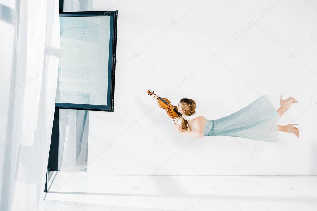 floating girl in blue dress playing violin near window 