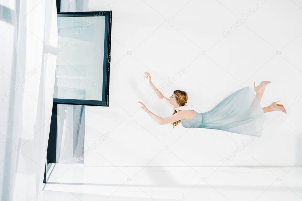 floating girl in blue dress raised hands near window with copy space