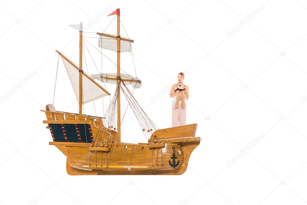 girl in pyjamas holding teddy bear and standing on floating ship model 