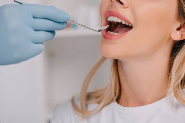partial view of dentist examining teeth of young woman with mouth mirror clipart