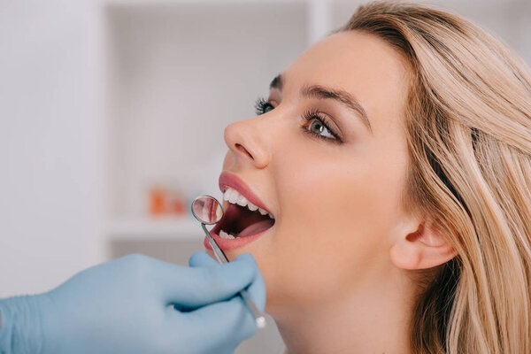 dentist examining teeth of young woman with mouth mirror