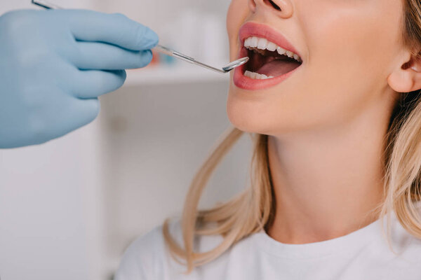partial view of dentist examining teeth of young woman with mouth mirror