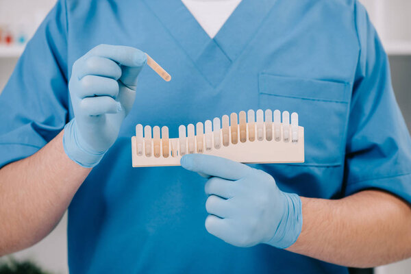 cropped view of dentist holding teeth color palette in clinic, teeth whitening concept