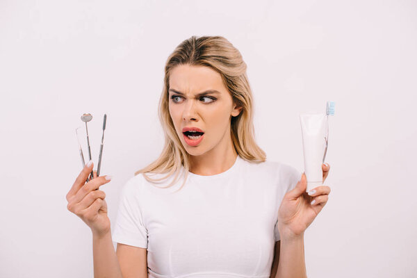 beautiful shocked woman holding toothpaste, toothbrush and dental instruments isolated on white