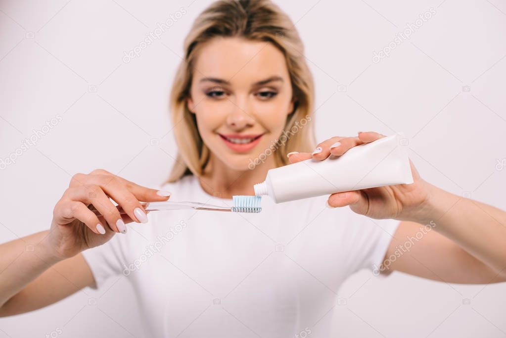 beautiful smiling woman putting toothpaste on toothbrush isolated on white