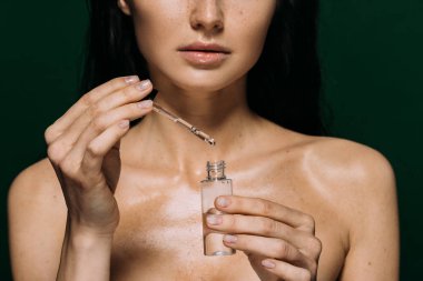 cropped view of naked woman holding bottle with serum isolated on green clipart