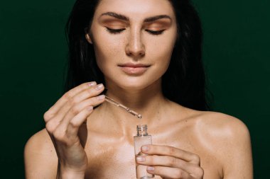 attractive naked woman holding bottle with moisturizing serum isolated on green clipart