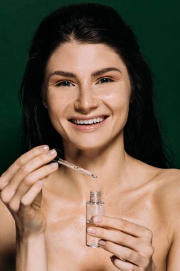 cheerful naked girl holding bottle with moisturizing serum isolated on green clipart
