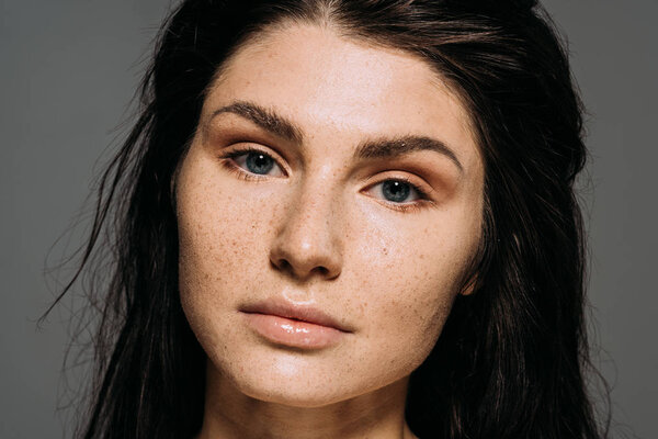 attractive brunette young woman with freckles on face isolated on grey