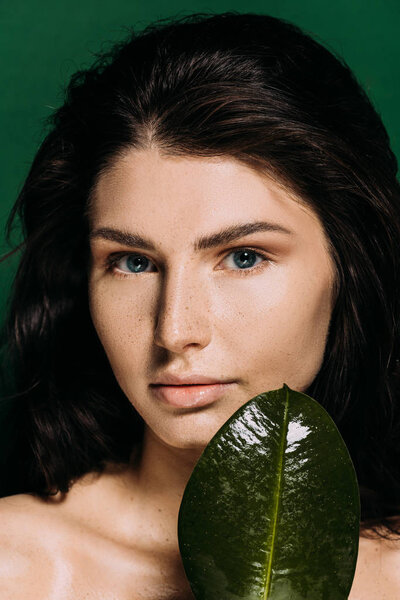 Portrait of beautiful tender girl with freckles on face posing with leaf isolated on green