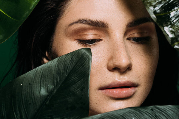 tender young woman with freckles posing with green leaves