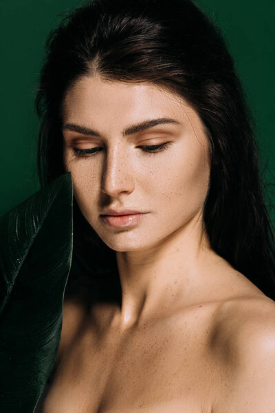 Portrait of tender girl with freckles on face posing with green leaf isolated on green