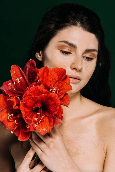 beautiful tender girl with freckles on face posing with red amaryllis flowers, isolated on green