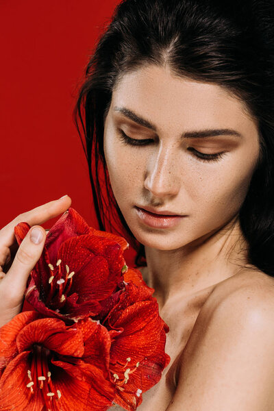 attractive tender young woman holding amaryllis flowers, isolated on red 