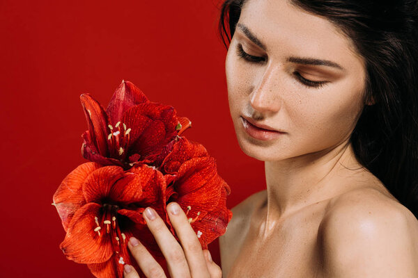 Portrait of tender young woman looking at amaryllis flowers, isolated on red
