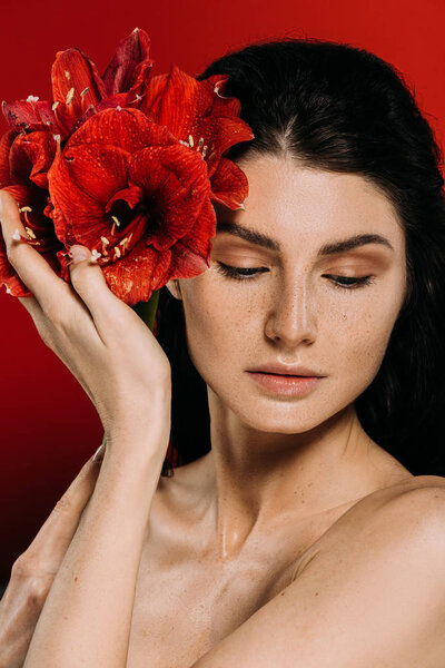 beautiful woman with freckles on face posing with amaryllis flowers, isolated on red
