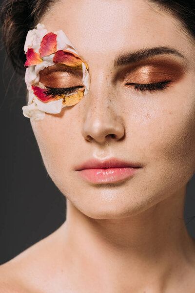 beautiful young woman with petals and makeup on closed eyes isolated on grey