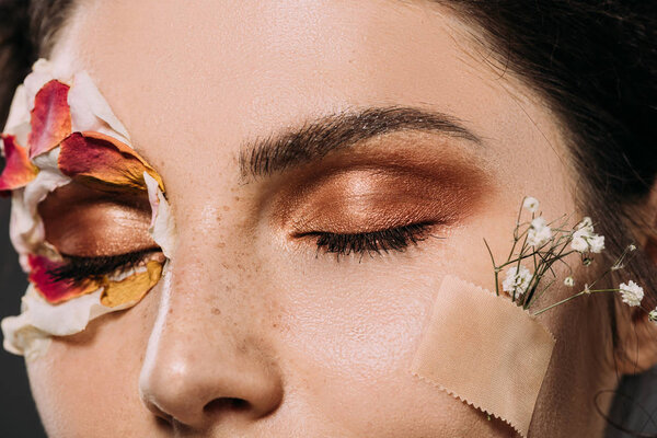 close up of woman with makeup on closed eyes and flowers on face 