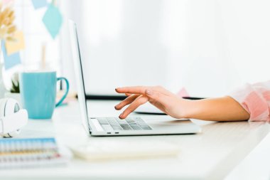 Partial view of woman typing on laptop keyboard at workplace clipart