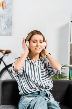 Çekici kadın kanepede oturan ve müzik dinleme çizgili gömlekli