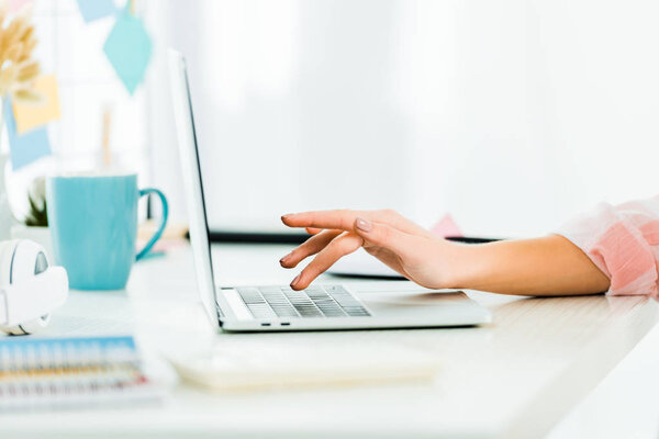 Partial view of woman typing on laptop keyboard at workplace