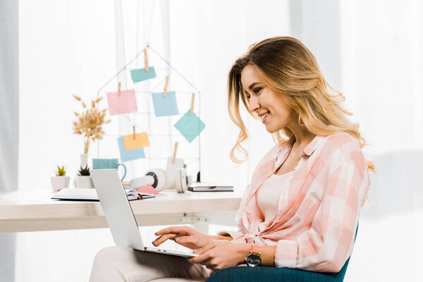 Smiling blonde woman in checkered shirt typing on laptop keyboard