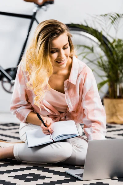 穿着格子衬衫的女人坐在地毯上 微笑着使用笔记本电脑 — 图库照片
