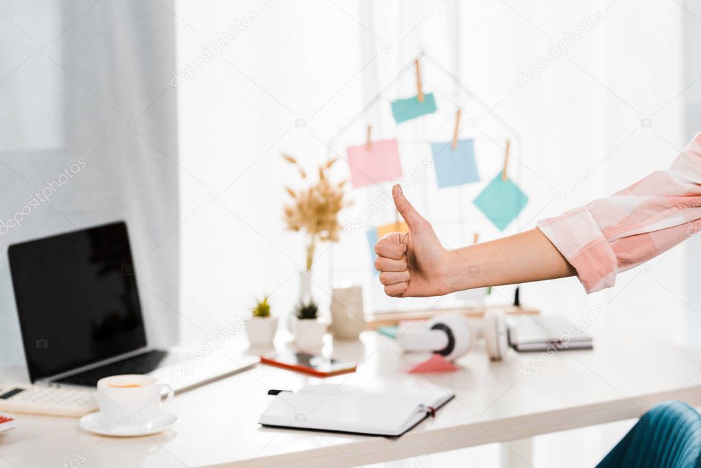 Partial view of woman showing thumb up at workplace