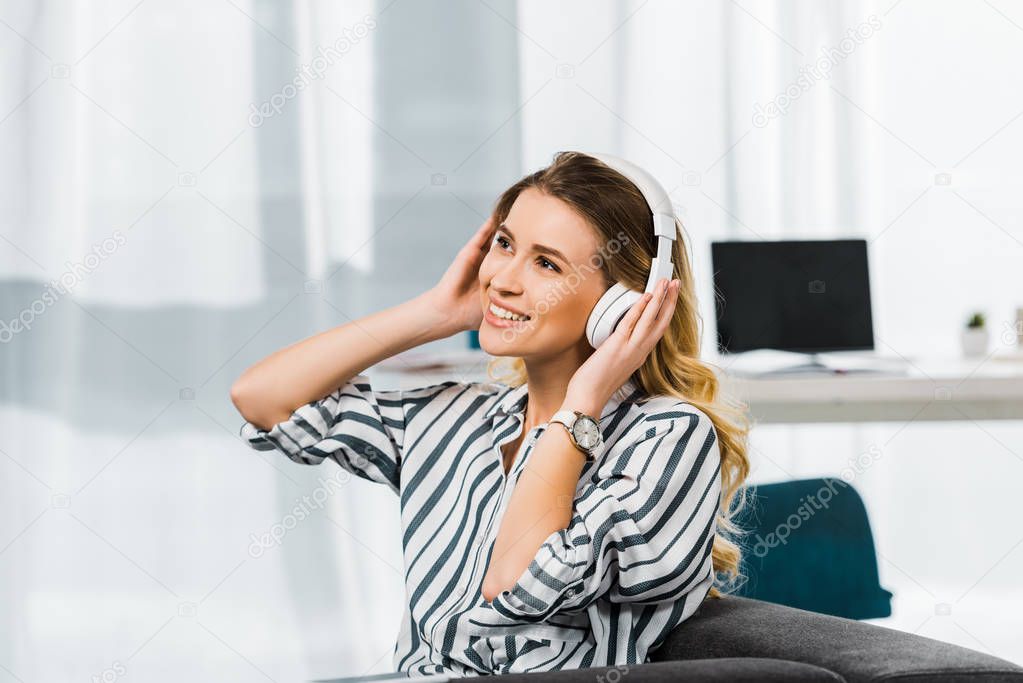 Happy woman in striped shirt sitting on sofa and listening music in headphones
