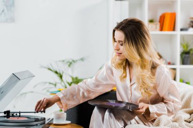 Vinil kayıt tutarak ve gramofon kullanarak pijama kıvırcık kadın