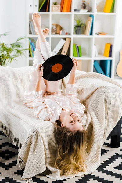 裸足でリラックスしてビニール レコードとソファーに横になっているパジャマの女性 — ストック写真