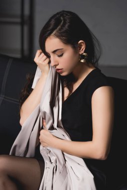 koyu arka plan üzerinde oturan siyah şık elbiseli çekici esmer kadın